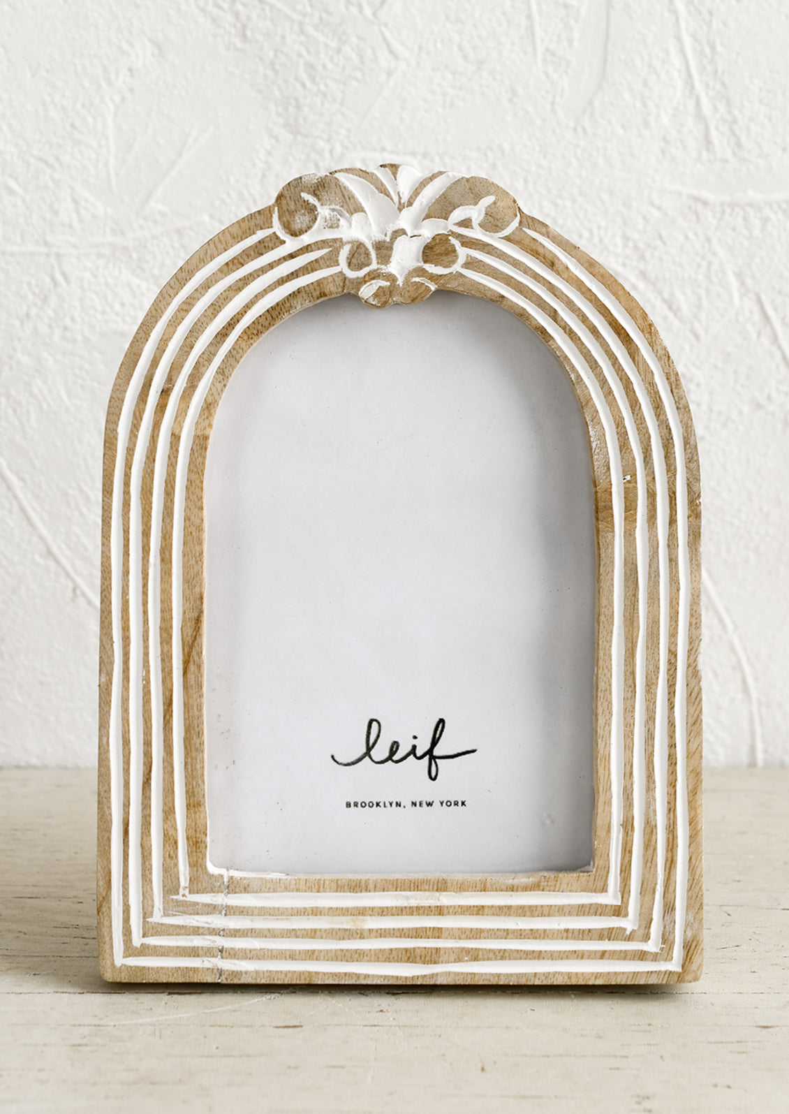 An arch shaped wooden picture frame with white paint detailing.