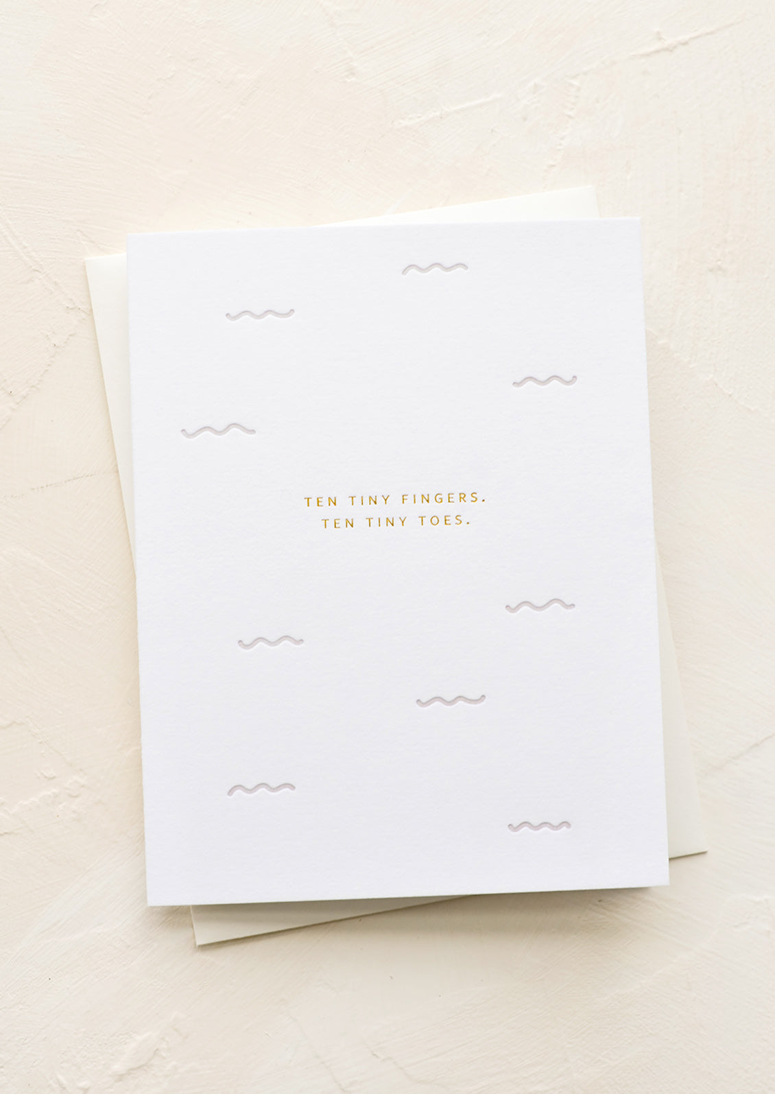 A greeting card with small gold letters reading "Ten tiny fingers, ten tiny toes".