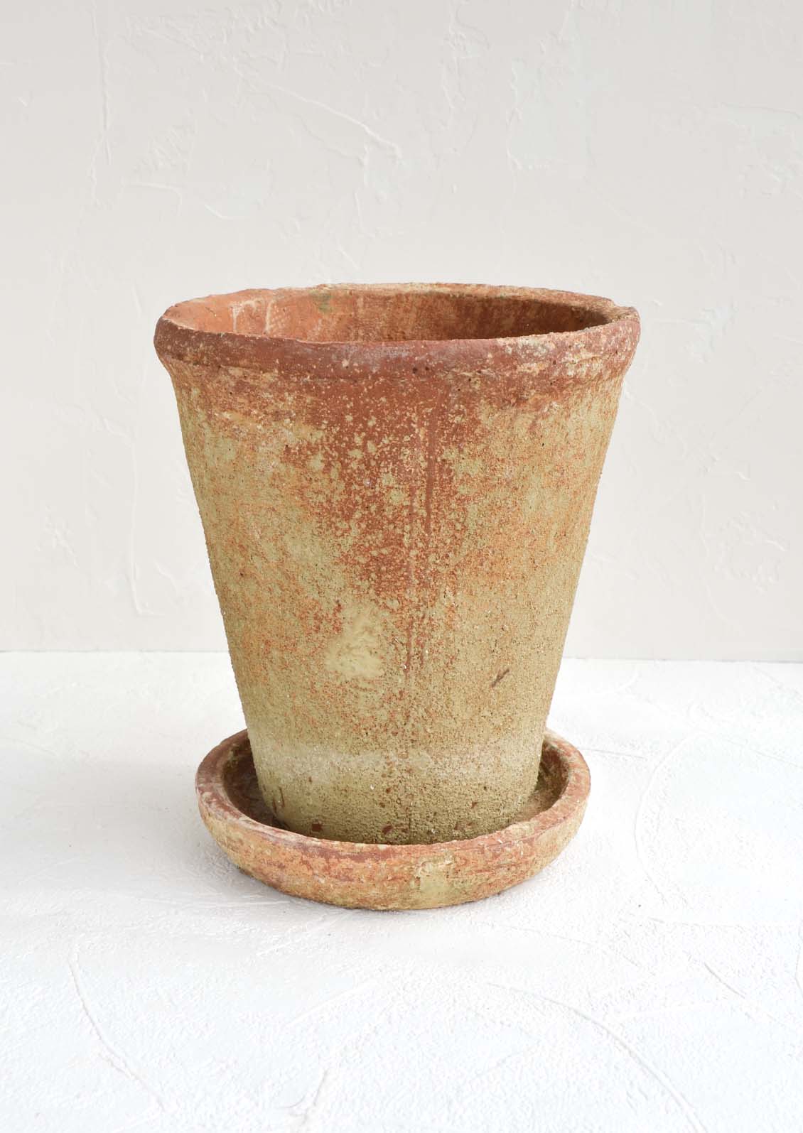 A rustic, heavily textured terracotta clay planter with saucer.