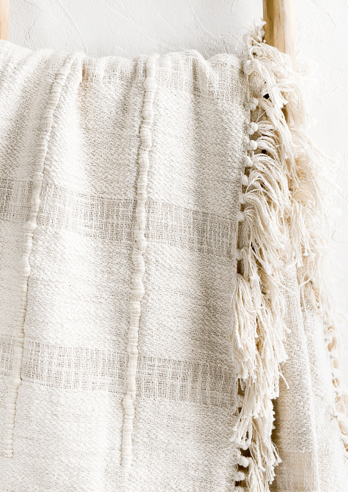 A natural cotton throw with paneling detailing and fringed trim.