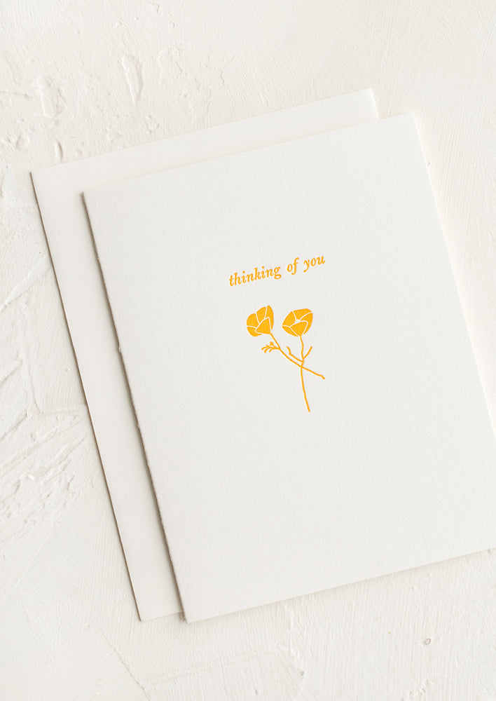 A white greeting card with yellow floral stems and "Thinking of you" text.