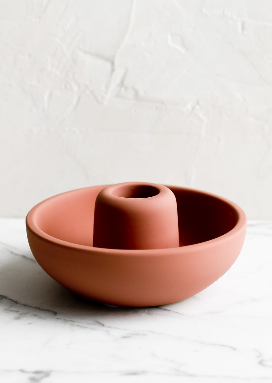 A matte taper candle holder with bowl-like base in dusty terracotta.