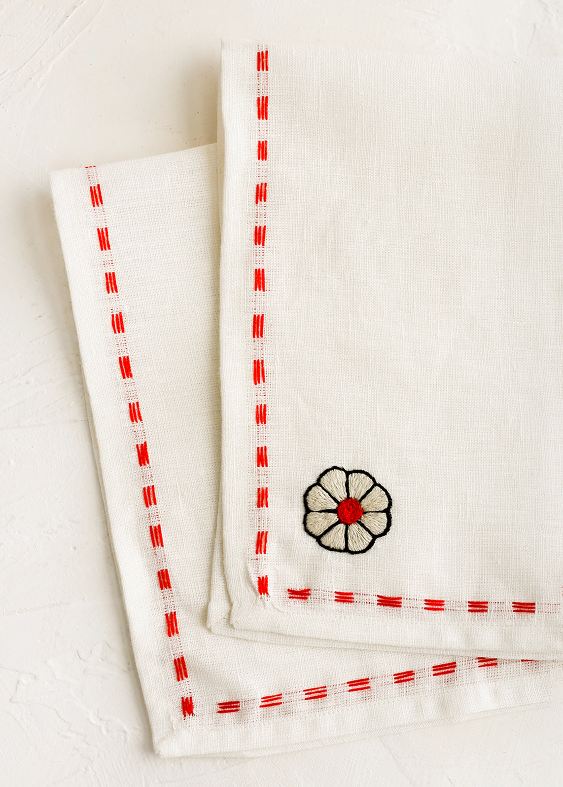 A white linen napkin with embroidery detailing in red.
