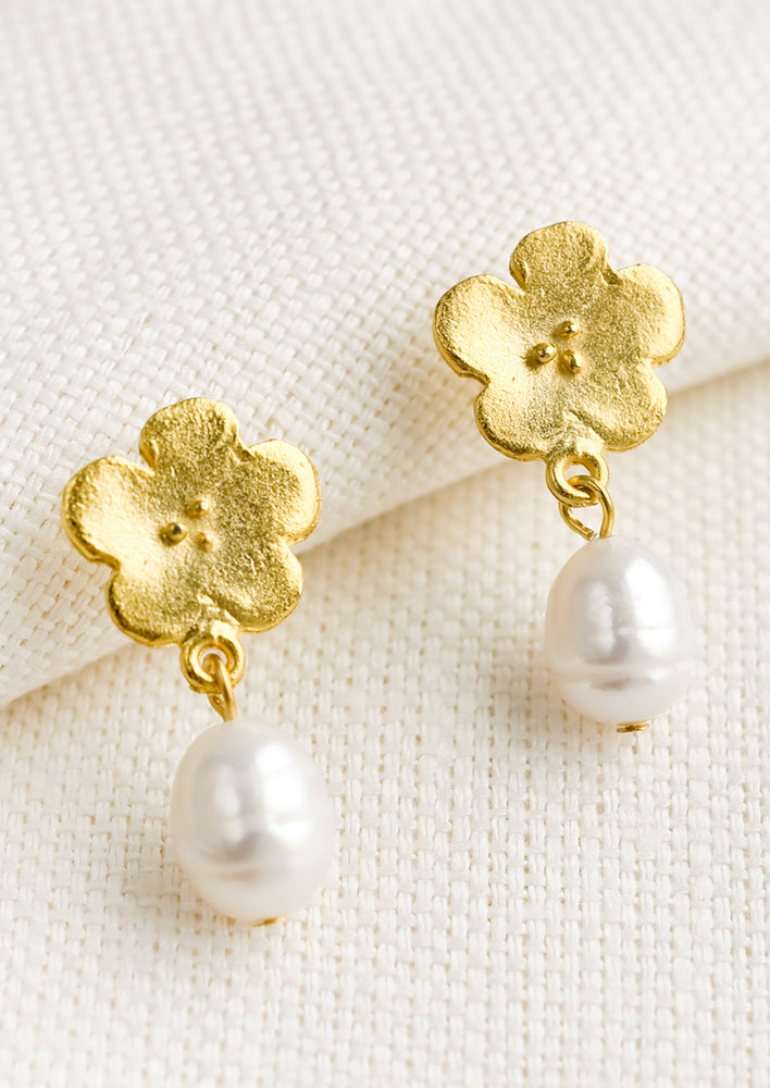A pair of earrings with gold flower post and pearl bead.