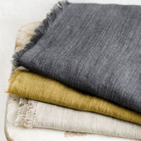 Ashen: A stack of frayed edge linen table runners in three different colors.