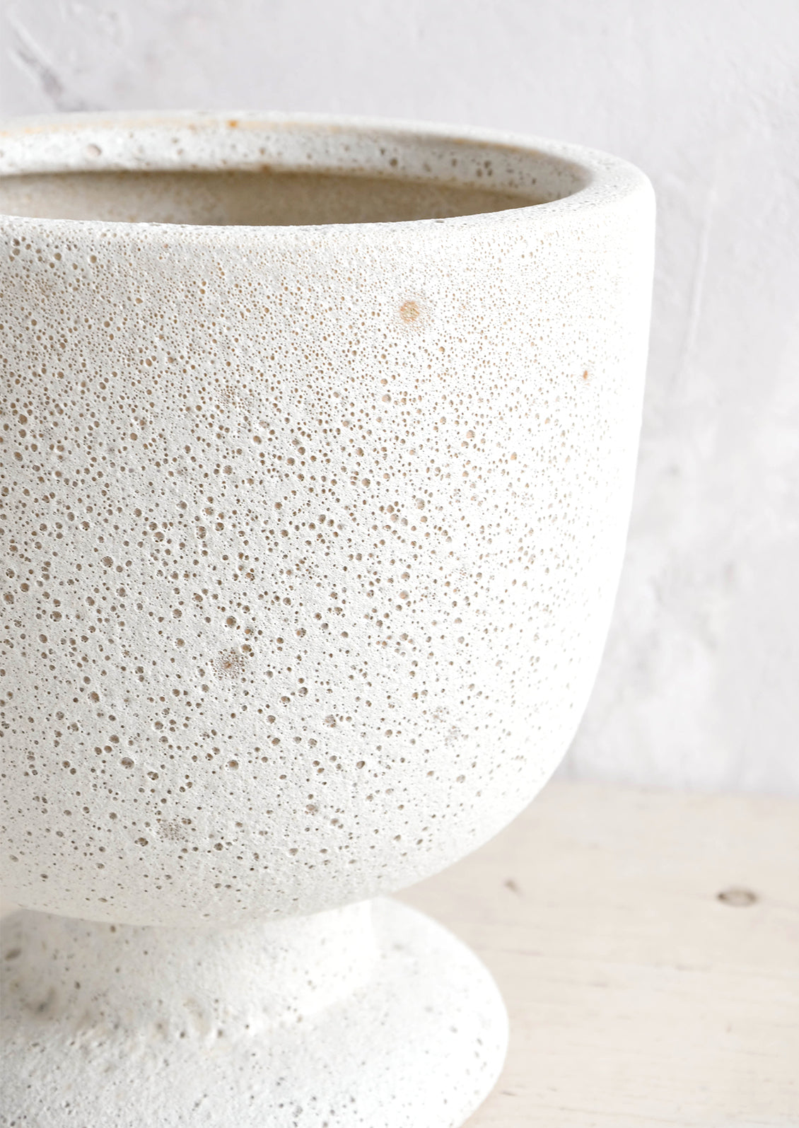 A planter in matte light grey textured glaze and footed urn shape.