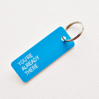 You're Already There: Small acrylic keychain, blue background with white words that says "YOU'RE ALREADY THERE"