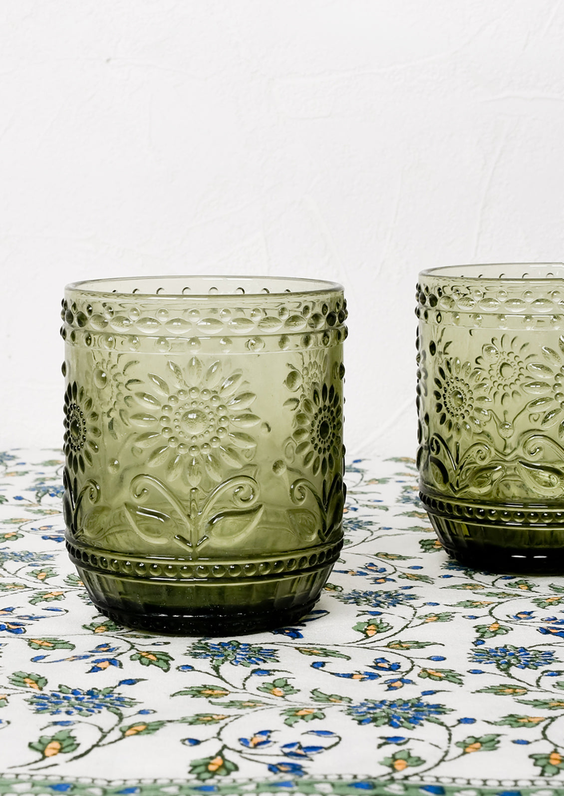 A pair of olive green glass tumblers with floral embossed motif.