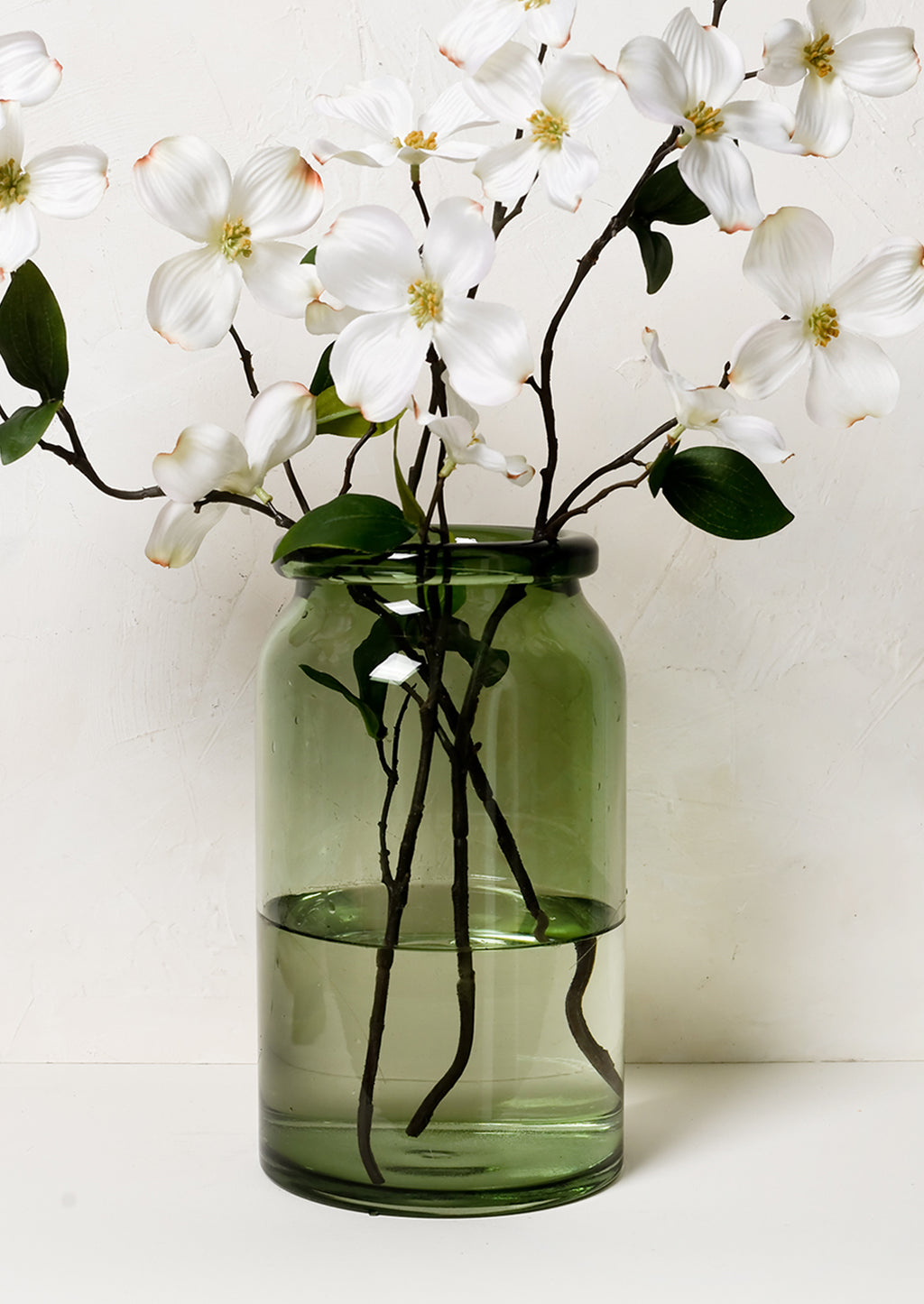 1: A tall green glass vase with dogwood branches.