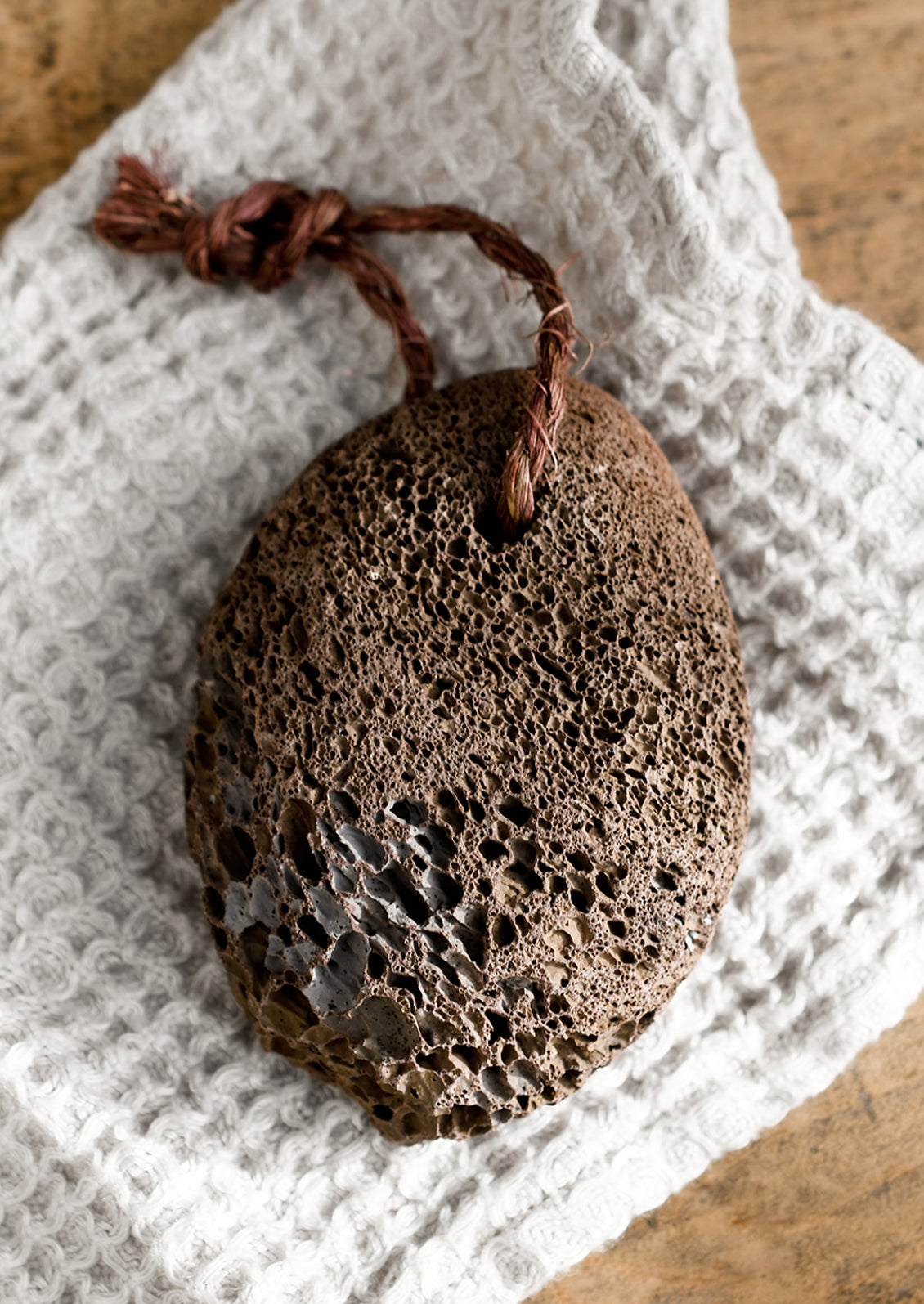 A dark brown natural pumice stone with twine tie.