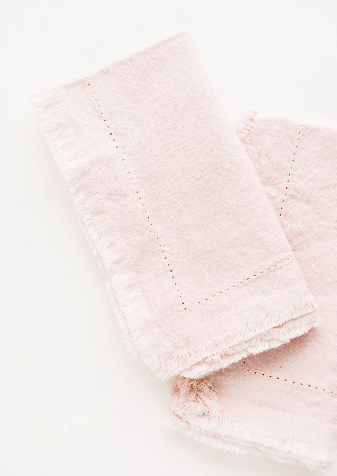 Two folded pink Cotton Napkins with frayed edges .