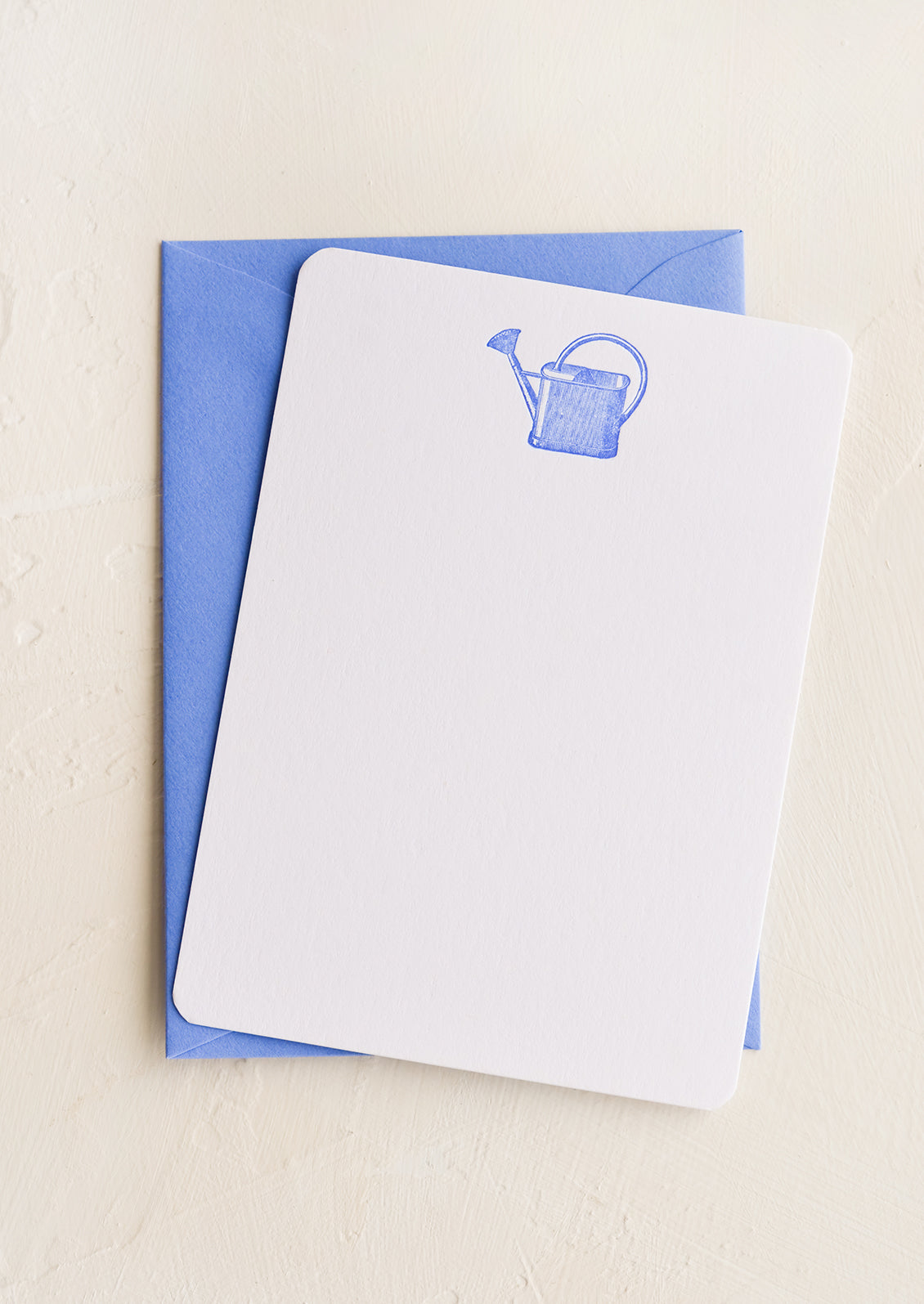 A white notecard with blue watering can letterpress printed at top, with blue envelope.