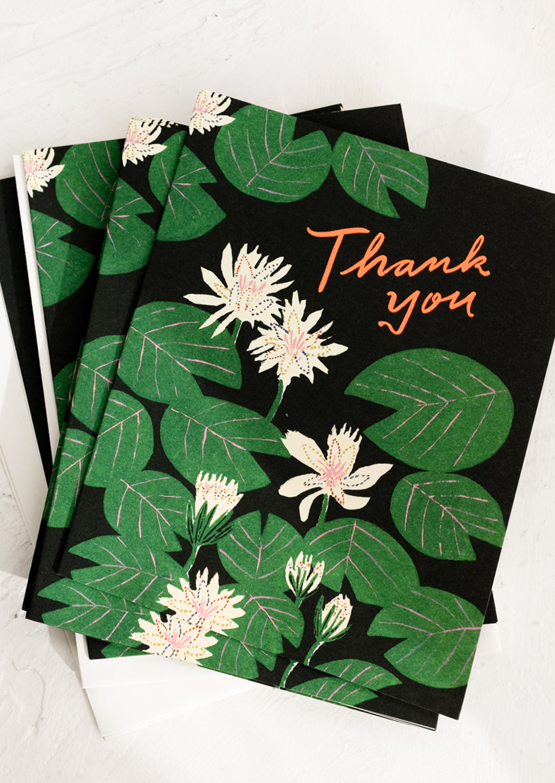 A set of water lily print thank you cards with black background and orange text reading "Thank you".