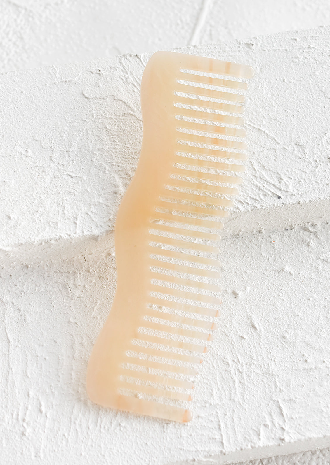 A wavy shaped acetate comb in peach.