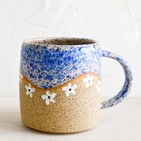 Blue / White: A speckled ceramic coffee mug in blue with wavy line of ivory daisies at middle.