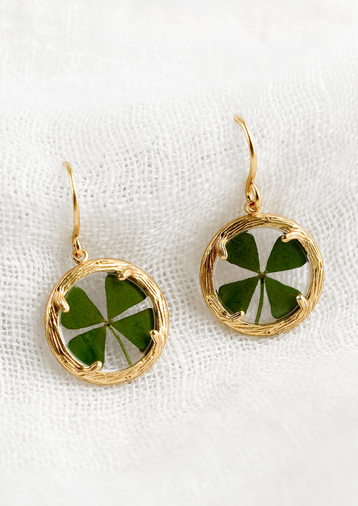 1: A pair of round earrings with gold frame around four leaf clover.