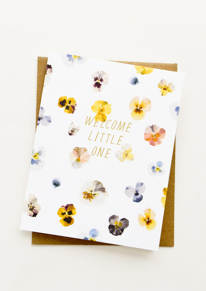 1: Greeting card with watercolor painted pansy flowers and gold text at center reading "Welcome Little One"