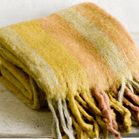 Wheat Multi: A fuzzy throw blanket with exaggerated fringe in wheat multi.