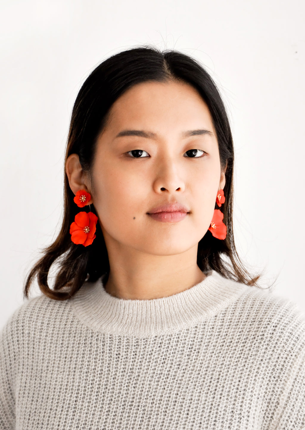 5: Model wears poppy red flower earrings and gray sweater.