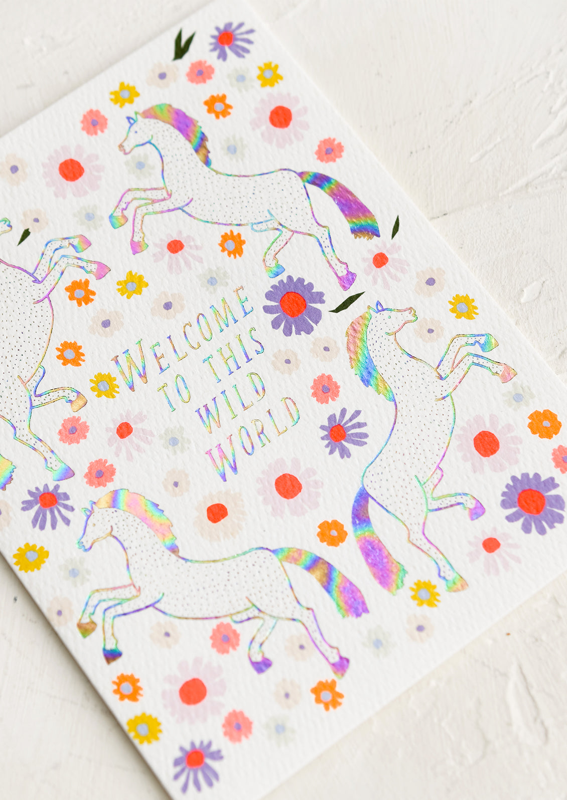 A greeting card with unicorn floral print, text reads "Welcome to this wild world".