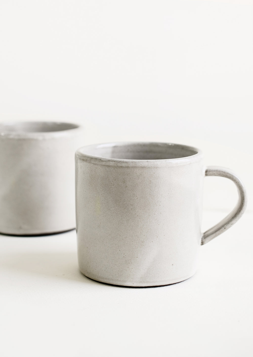 3: Two identical ceramic coffee mugs in a simple, classic shape in a white glaze over brown clay.