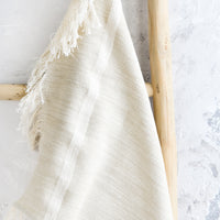 2: A woven kitchen towel in white hanging on a ladder.