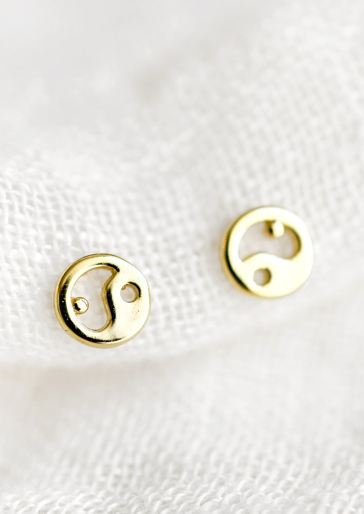 A pair of gold stud earrings in shape of yin yangs.