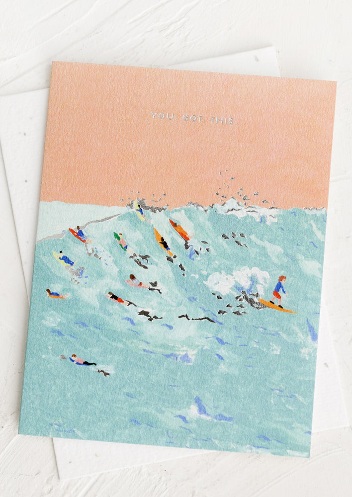 A greeting card with an image of surfers in the ocean, small silver text at top reads "You got this".