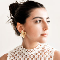 2: Model wears gold flower-shaped earrings and white top.