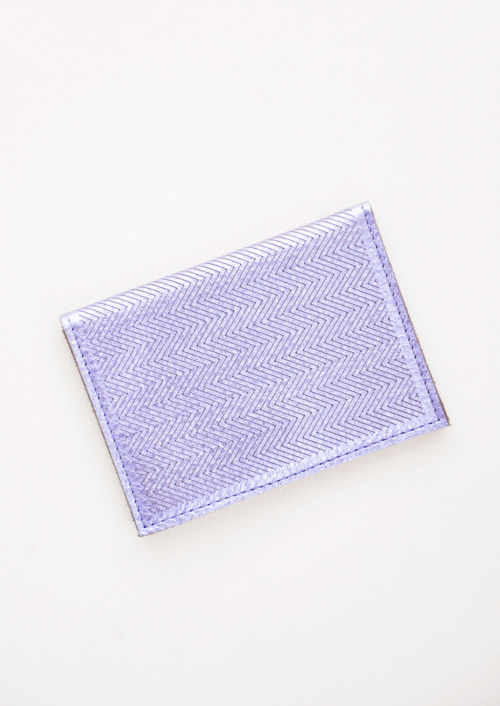 Metallic Periwinkle: Slim metallic blue leather wallet with two interior slip pockets that folds closed with a snap, shown closed with zig zag etched pattern. 
