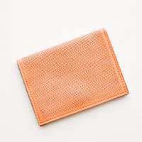 Terracotta: Slim terracotta orange leather wallet with two interior slip pockets that folds closed with a snap, shown closed with zig zag etched pattern. 
