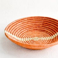2: Shallow, peach colored woven raffia bowl with natural streak across middle