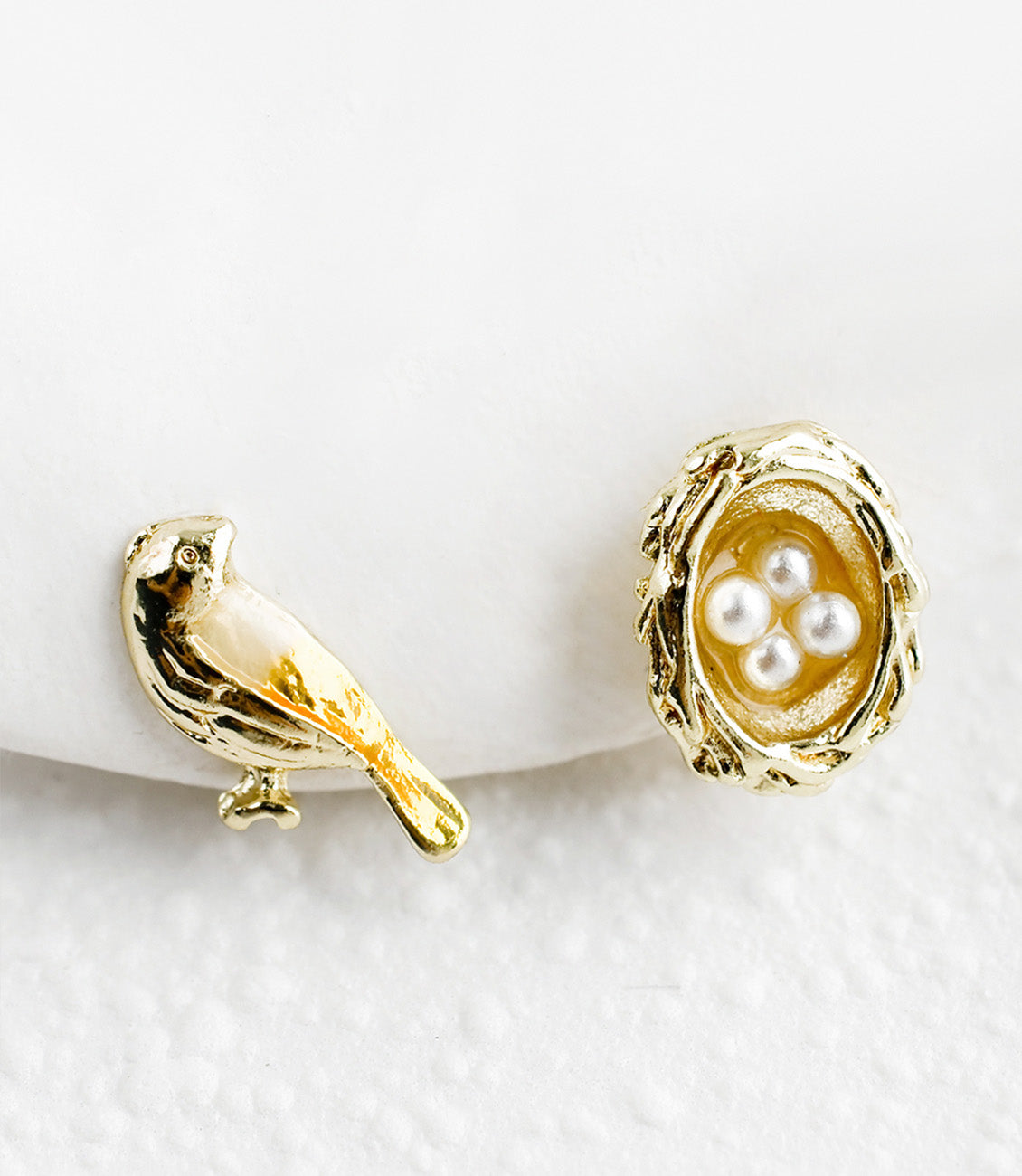 A pair of stud earrings, one bird and one nest with pearl eggs.