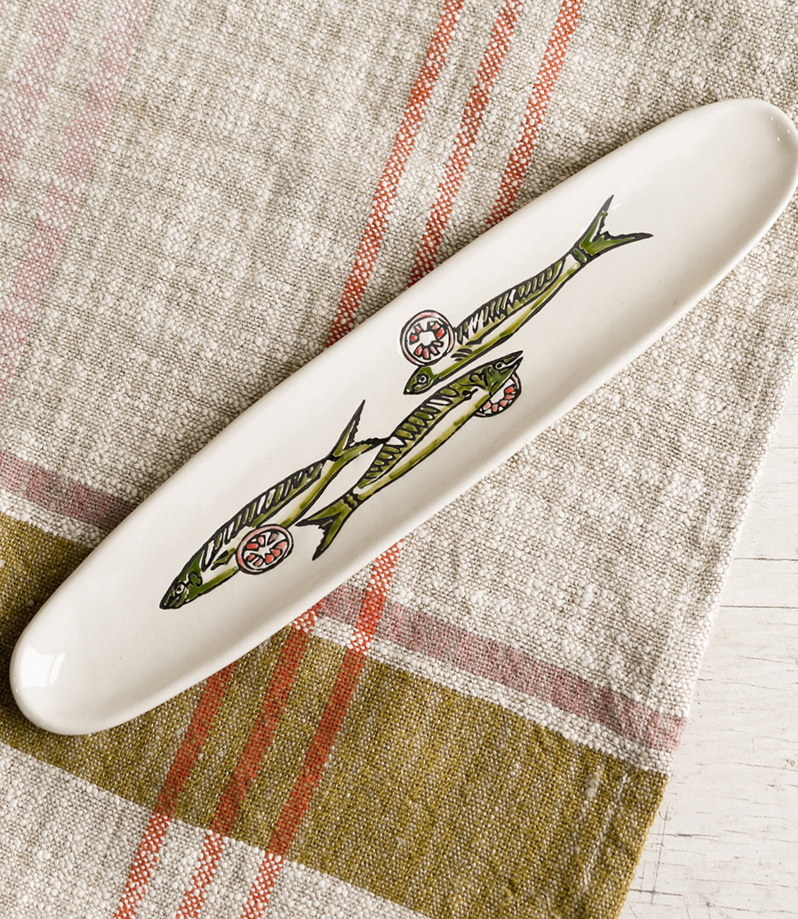 A long and skinny white ceramic dish with green sardine print.