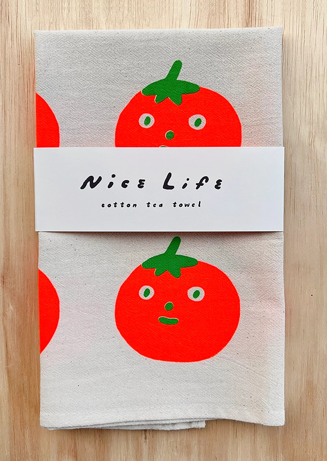 A folded tea towel with repeating anthropomorphic tomato motif.