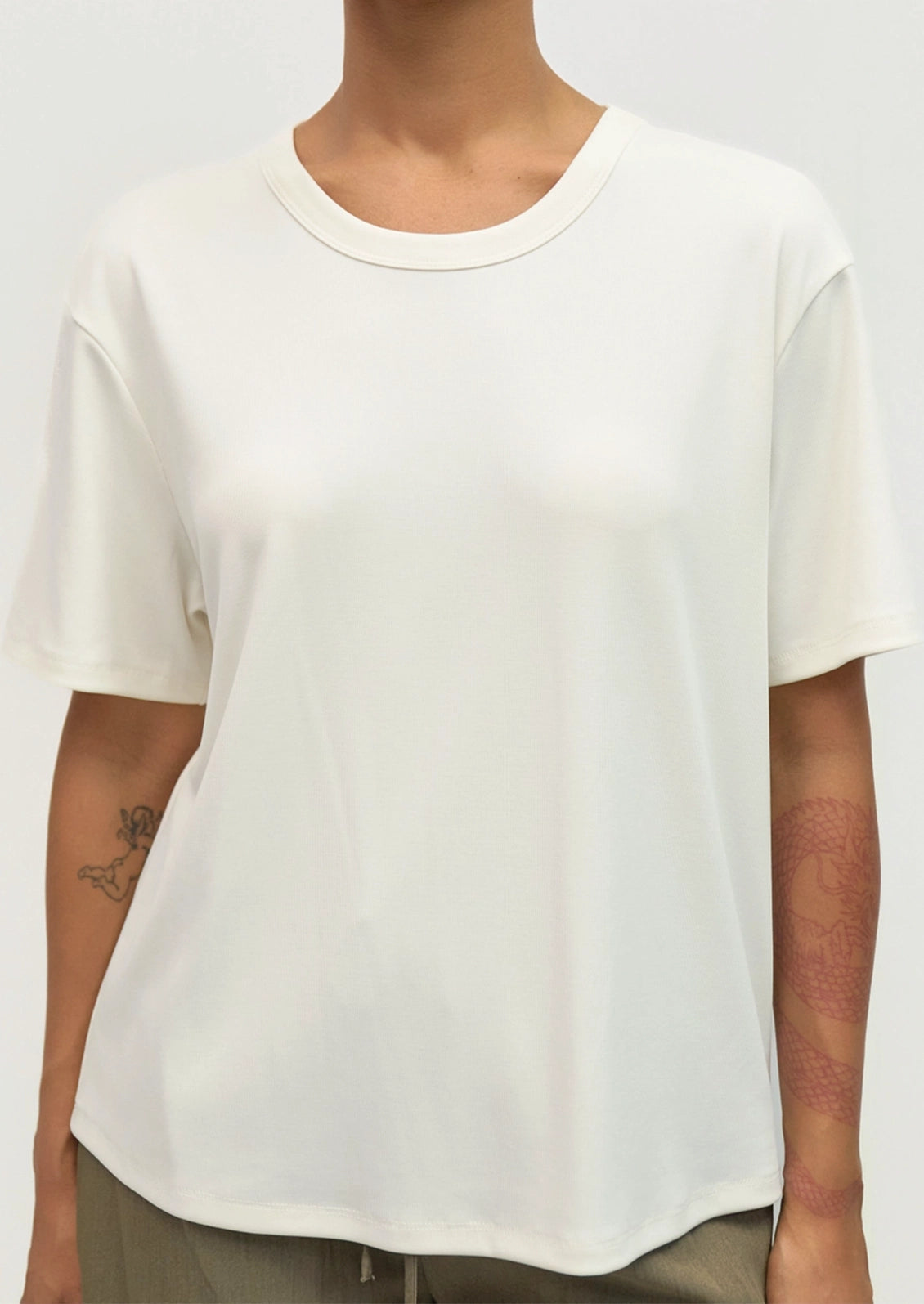 A person wearing a plain white short-sleeve crewneck t-shirt, cropped from the neck down, against a light gray studio background.