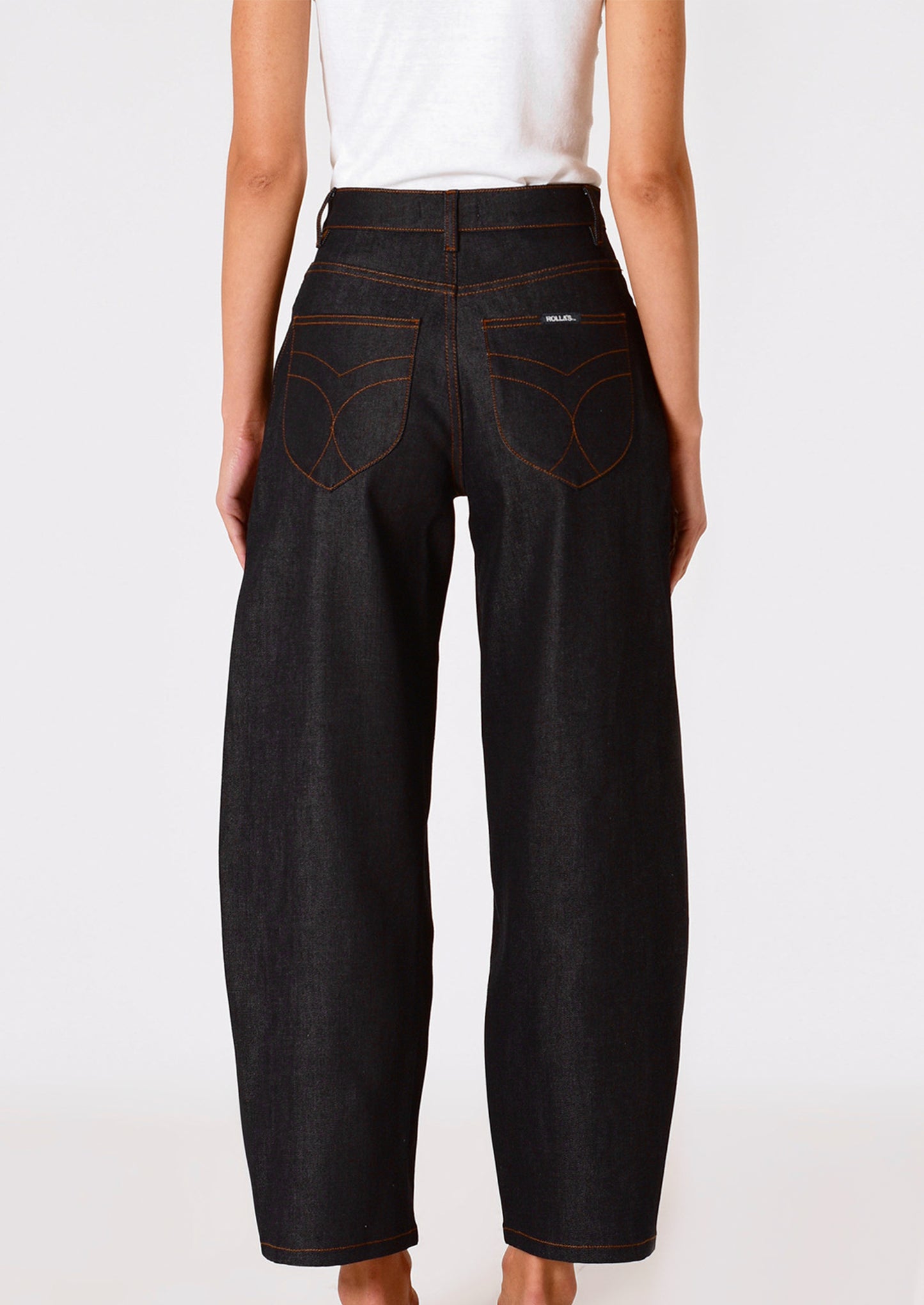 A person wearing a pair of dark rinse jeans with gold-tone exposed button fly and contrast orange stitching.