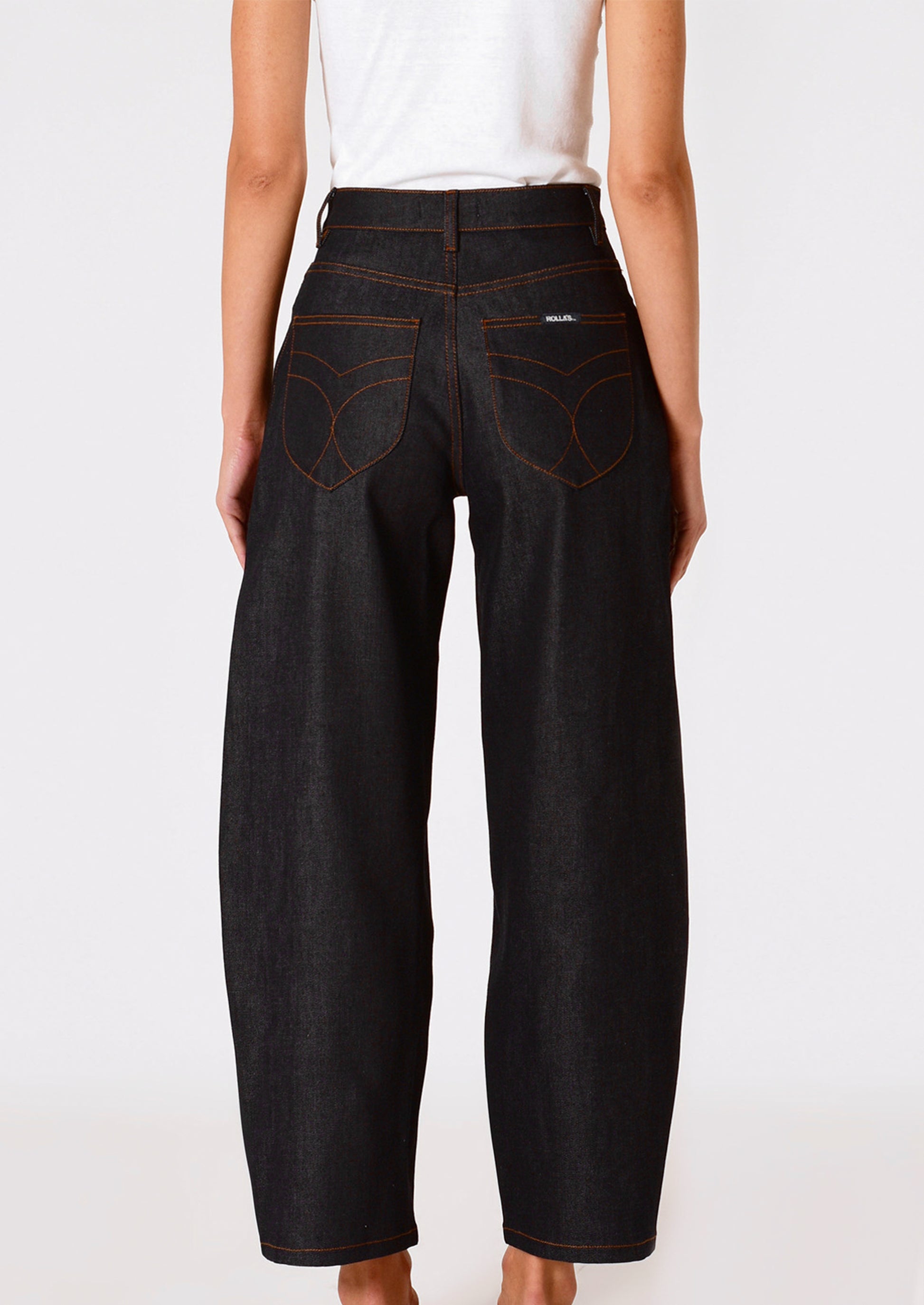 A person wearing a pair of dark rinse jeans with gold-tone exposed button fly and contrast orange stitching.