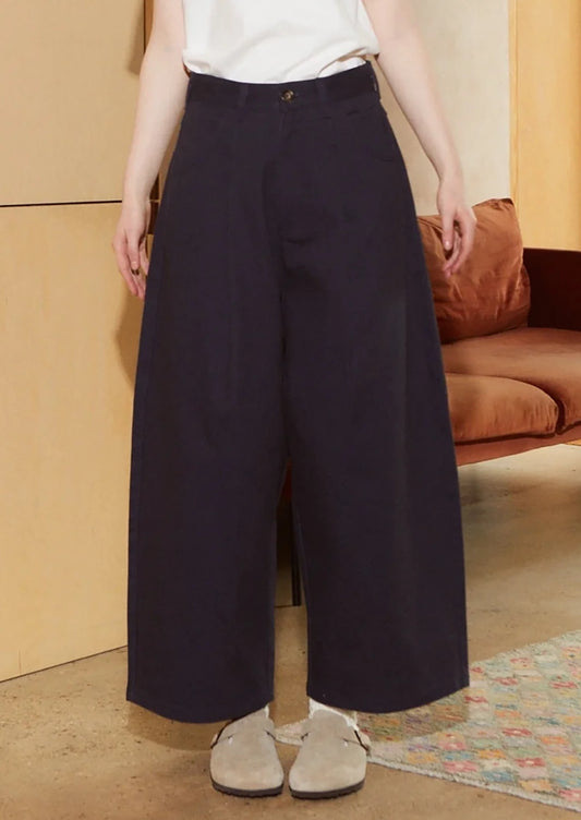 A woman wearing a pair of pleat front, balloon leg jeans in navy blue color.