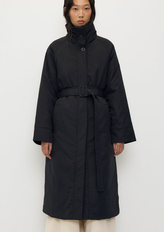 A person wearing a long black winter coat with matching belt.
