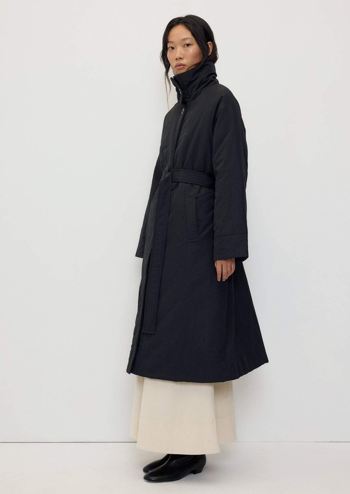A person wearing a long black winter coat with matching belt.