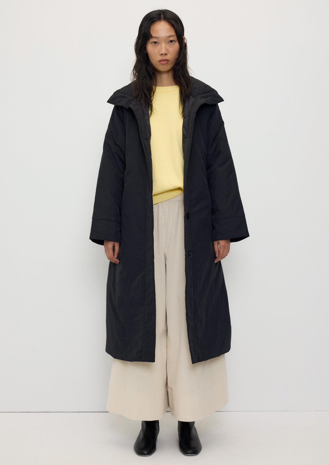 A person wearing a long black winter coat with matching belt.