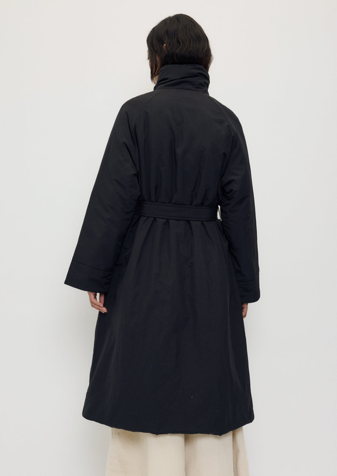 A person wearing a long black winter coat with matching belt.