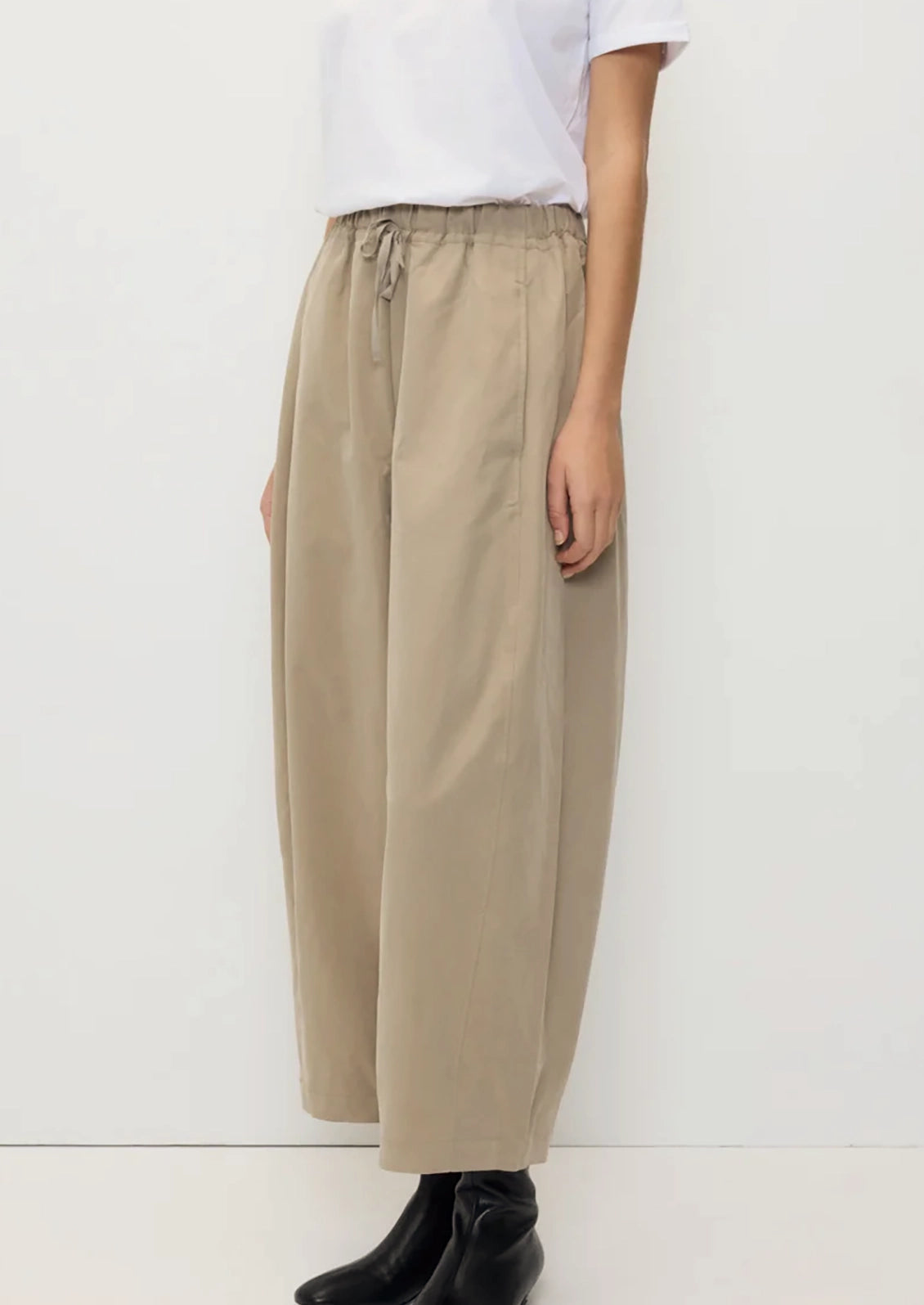 A person wearing a pair of tan barrel leg pants with elasticized drawstring waist.