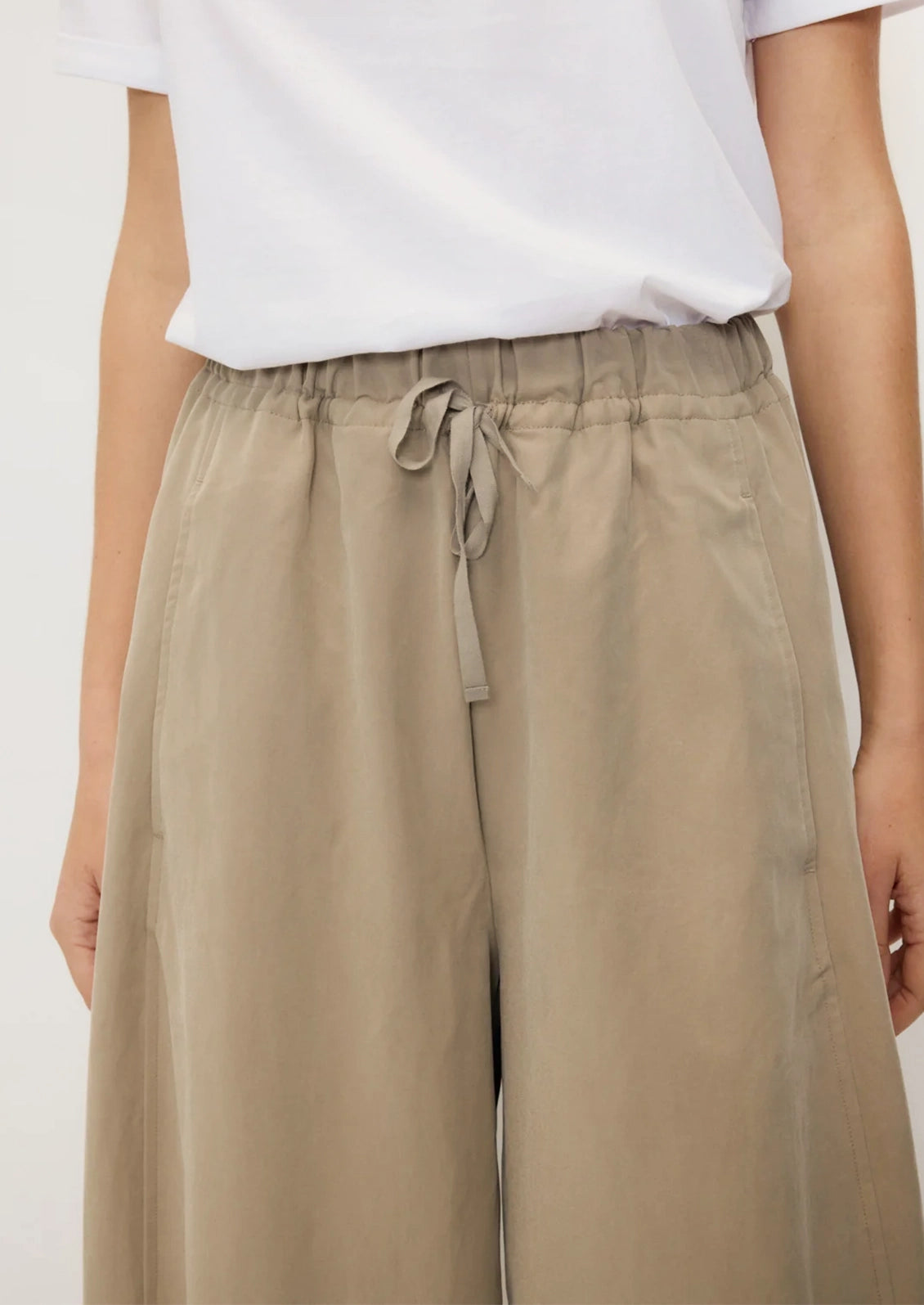 A person wearing a pair of tan barrel leg pants with elasticized drawstring waist.