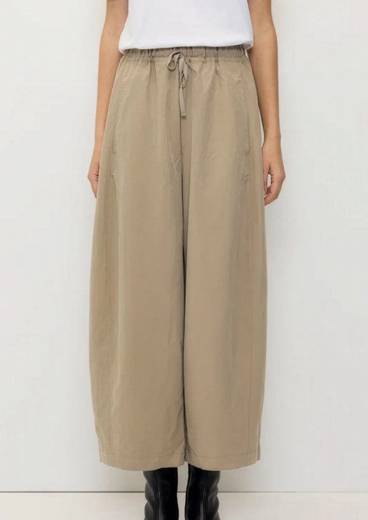 A person wearing a pair of tan barrel leg pants with elasticized drawstring waist.
