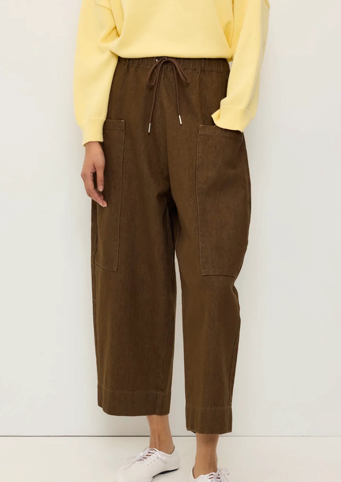 A person wearing a pair of brown denim pants with barrel leg shape and carpenter-style pockets.
