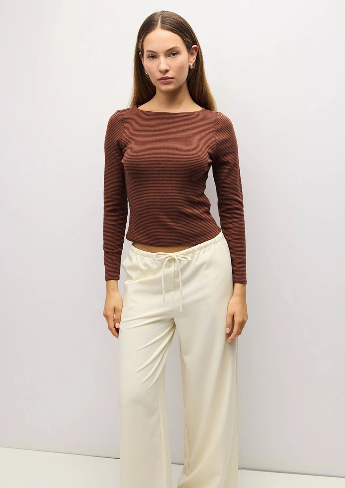 A person wearing a long sleeve boat neck fitted tee in brown and navy stripe.