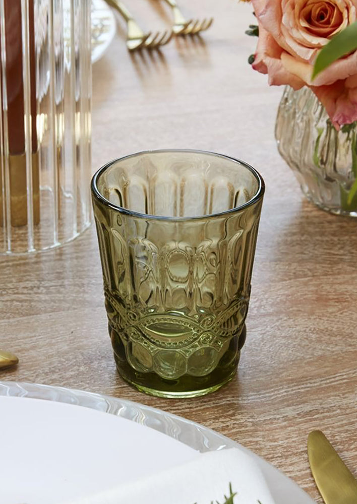 An olive green glass cup with vintage style embossed design.