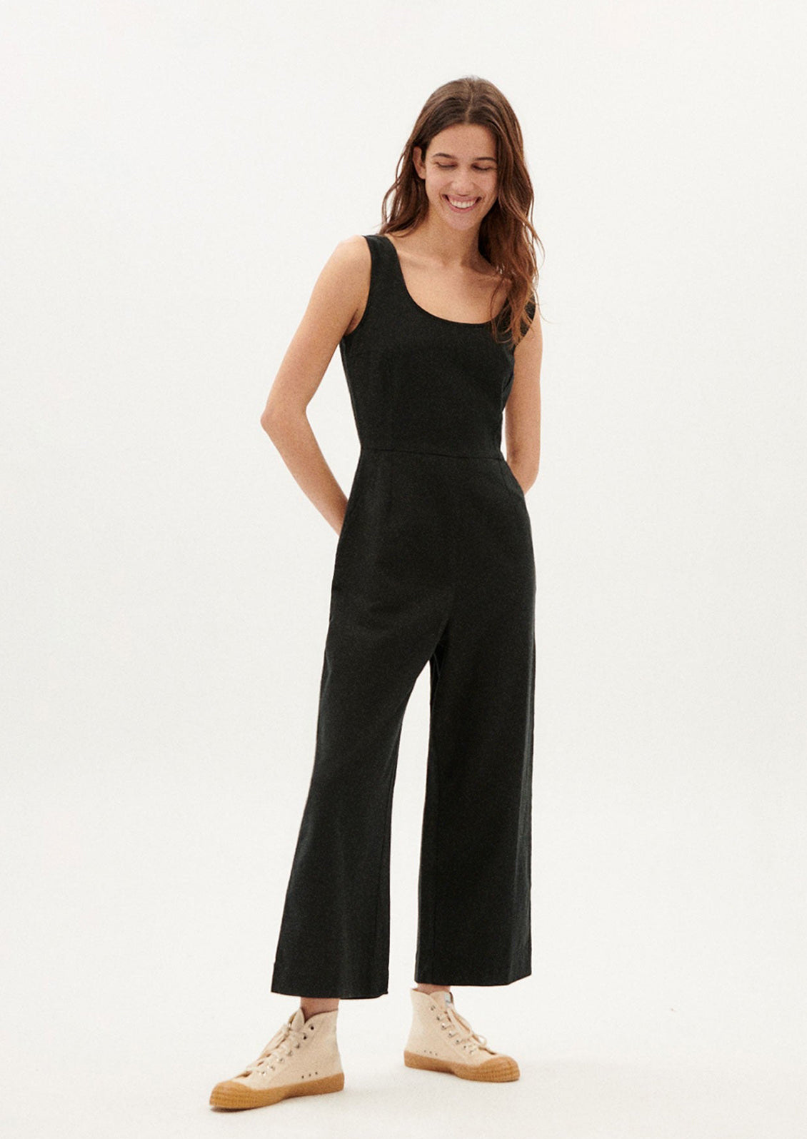 A woman wearing a black one piece jumpsuit with scoop neck.